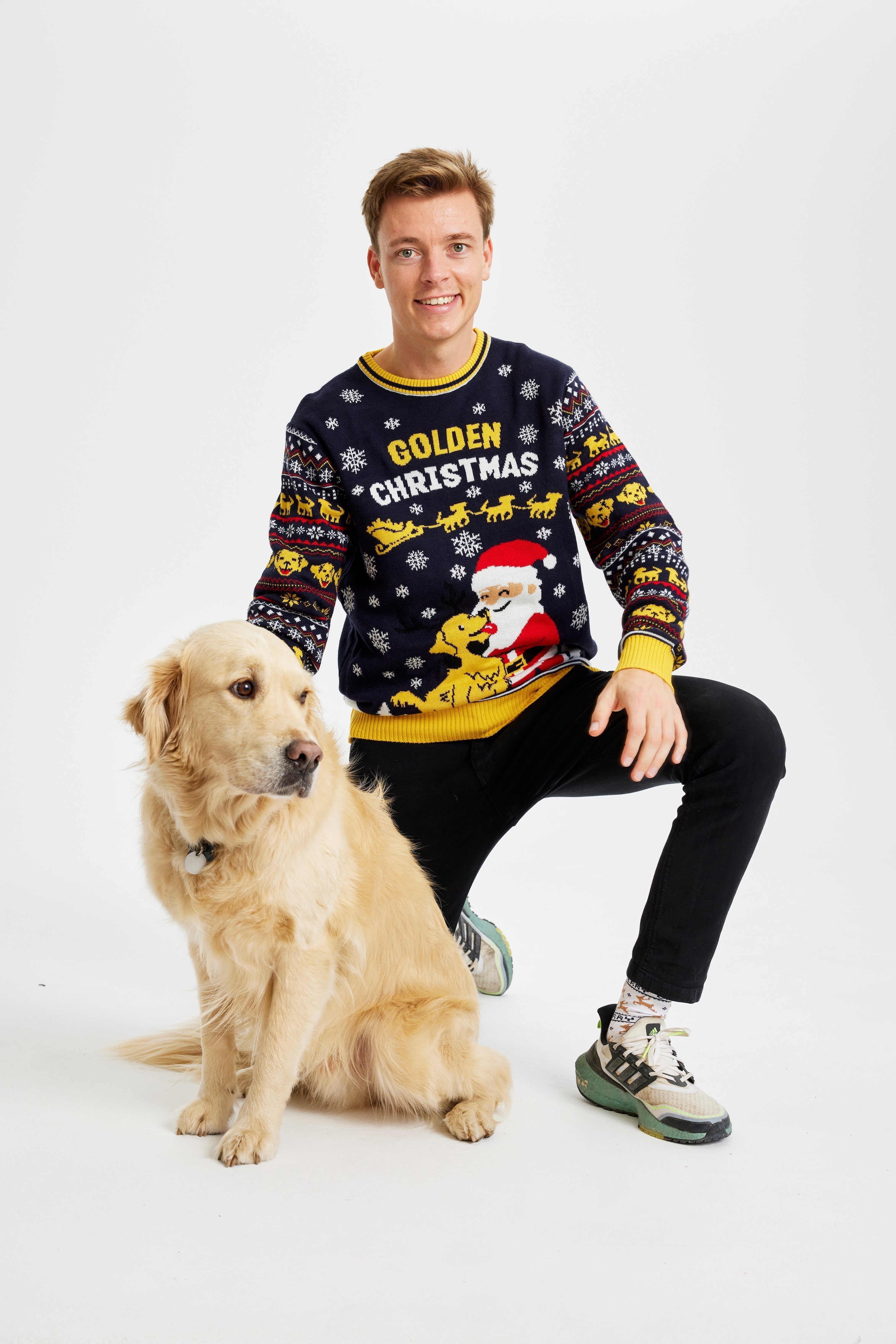 Un homme souriant avec un chien portant un pull de Noël jaune et noir avec la citation